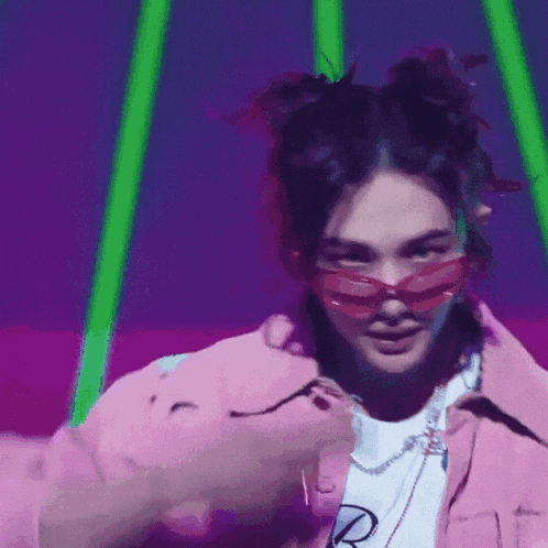 a woman wearing sunglasses and a pink jacket is dancing