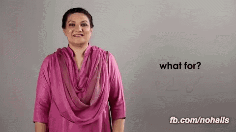 a woman in a pink shirt is standing in front of a gray wall and asking what for .