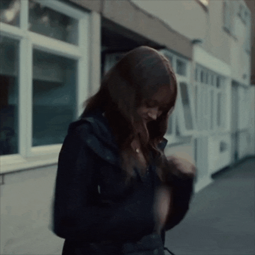 a woman in a black jacket is walking down a sidewalk