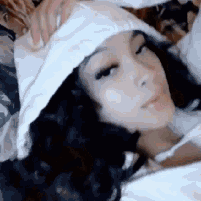 a woman is laying on a bed wearing a white hoodie and a white hat .