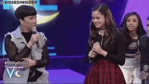 a woman is holding a microphone and talking to another woman on stage .