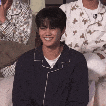 a young man wearing a blue pajama shirt smiles while sitting on a couch