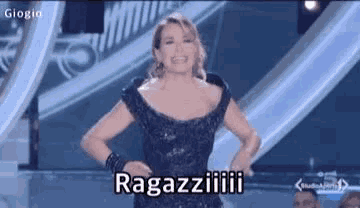 a woman in a black dress is standing on a stage with her hands on her hips .