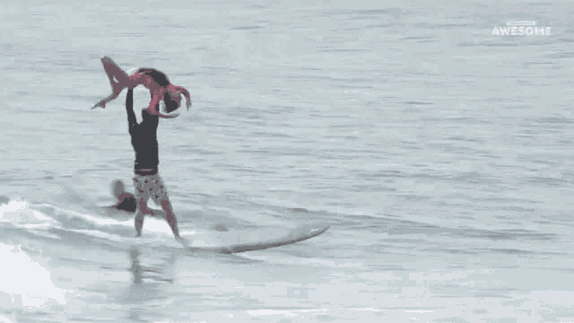 a man is holding a woman in the air while riding a wave