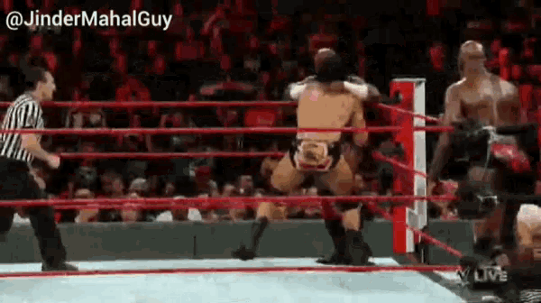 a referee is standing in the middle of a wrestling ring watching two men fight .