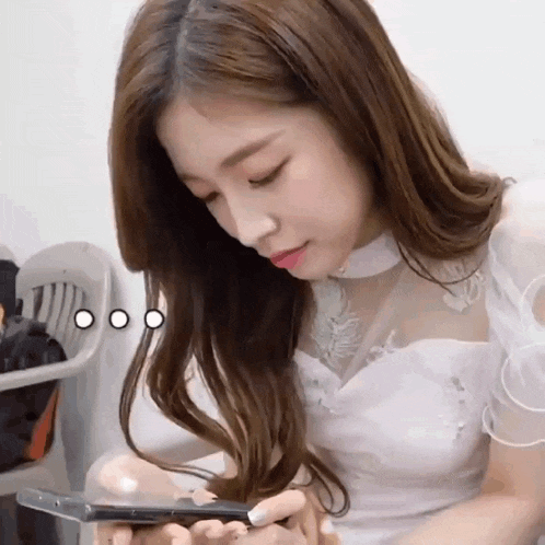 a woman in a white dress is looking at a cell phone