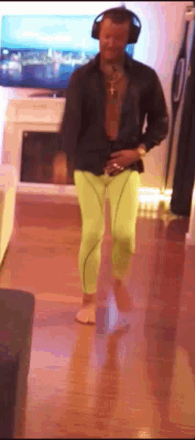 a man wearing headphones and neon green pants is walking in a living room .