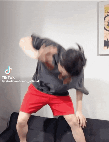 a man in a black shirt and red shorts is dancing on a couch with a tiktok watermark on the bottom