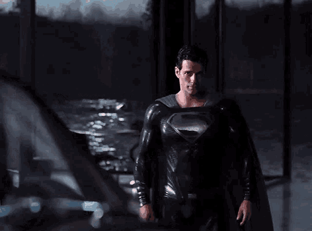 a man in a black superman costume is smiling while standing in front of a car .