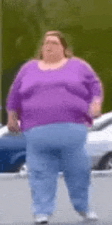 a very fat woman wearing a purple shirt and blue jeans is walking down the street .
