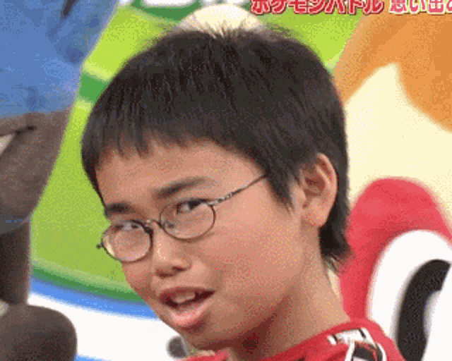 a young boy wearing glasses and a red shirt is looking at the camera .