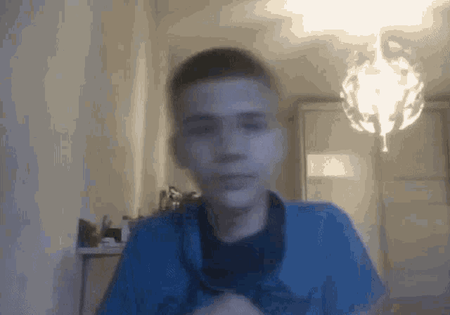a boy in a blue shirt is standing in front of a chandelier .