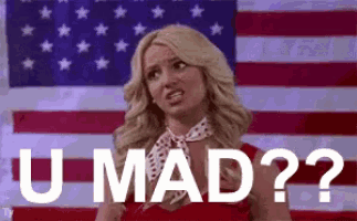 a woman is standing in front of an american flag with the words `` u mad '' written on her face .
