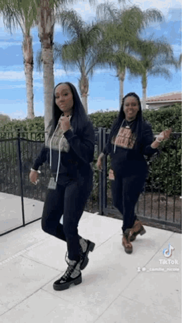 two women are dancing together in front of palm trees .