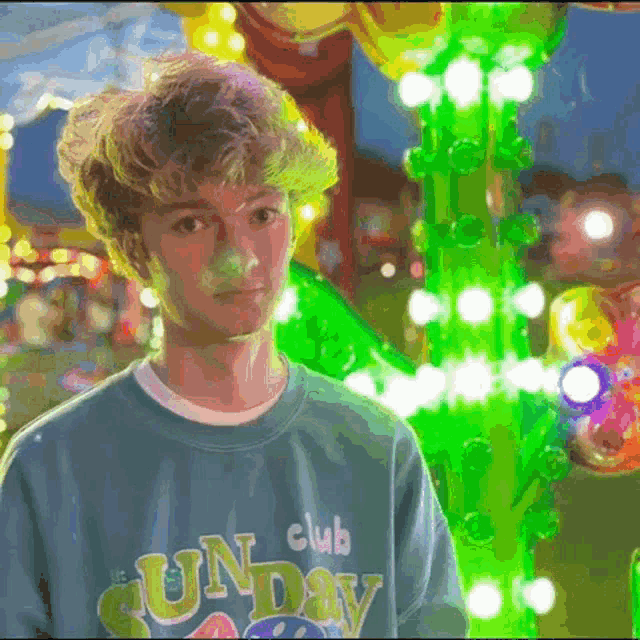 a boy wearing a club sunday sweatshirt stands in front of a carnival ride