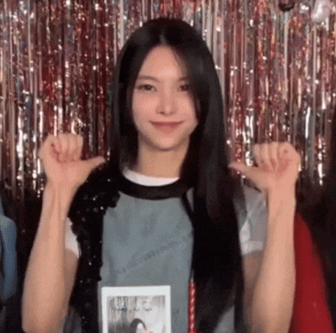 a young woman with long black hair is giving a thumbs up sign in front of a tinsel curtain .