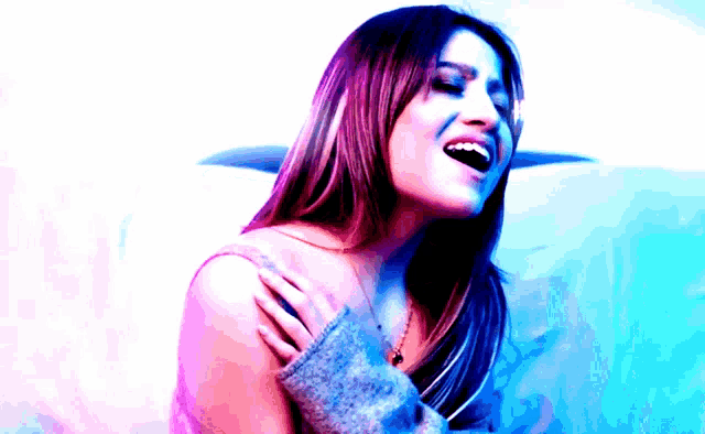 a woman in a sweater is singing into a microphone with a blue background