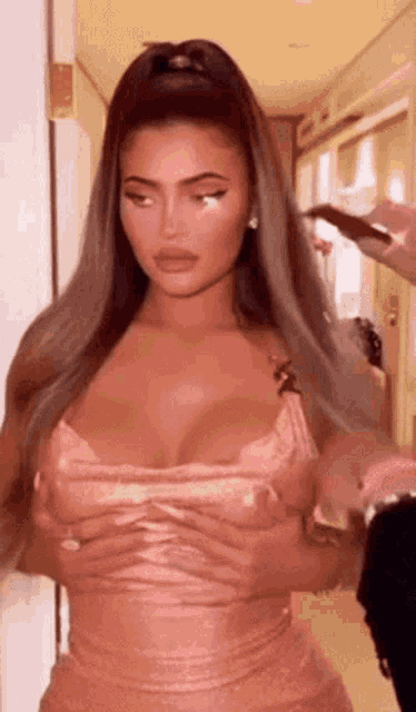 a woman in a pink dress is standing in a hallway holding her breasts .