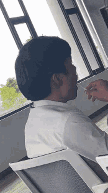 a man in a white shirt smoking a cigarette in front of a window