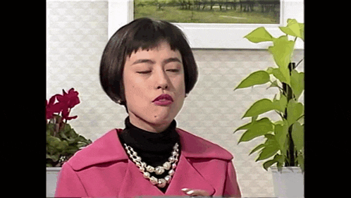 a woman wearing a pink coat and a pearl necklace