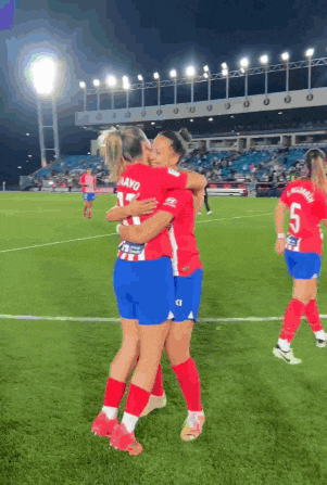 two female soccer players hugging on the field with one wearing the number 5 on her shorts