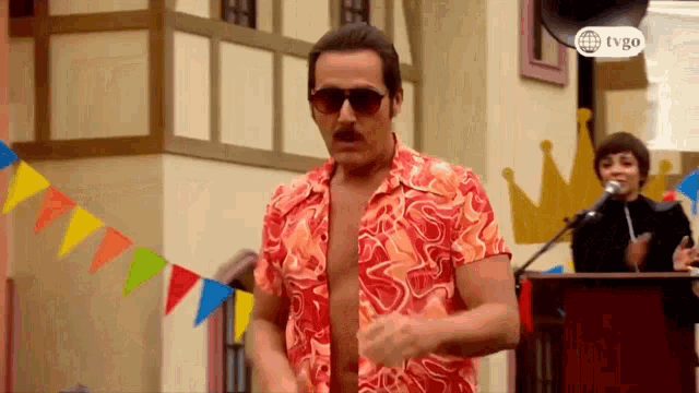 a man wearing sunglasses and a shirt without a shirt is dancing in front of a microphone .