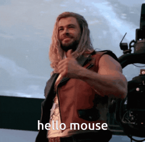 a man with long hair and a beard is giving a thumbs up and saying hello mouse