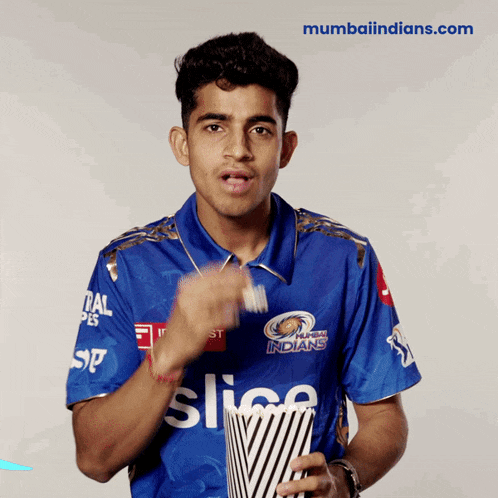 a man wearing a blue shirt that says mumbai indians is holding a bag of popcorn