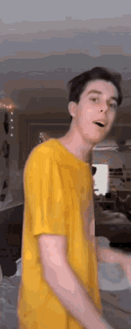 a young man wearing a yellow shirt is standing in a living room .