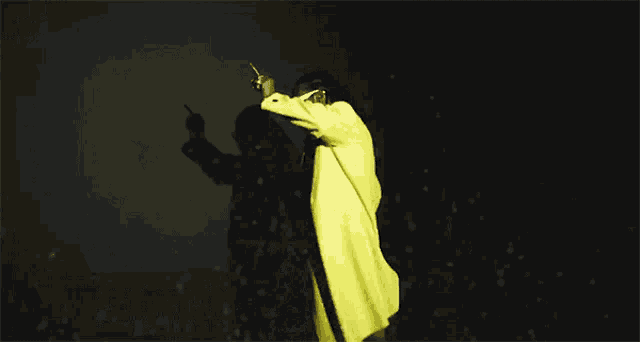 a person in a yellow coat is standing in the dark .