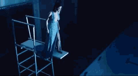 a woman in a blue dress is standing on top of a table in a dark room .