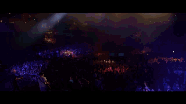 a group of people playing instruments on a stage with a large screen behind them