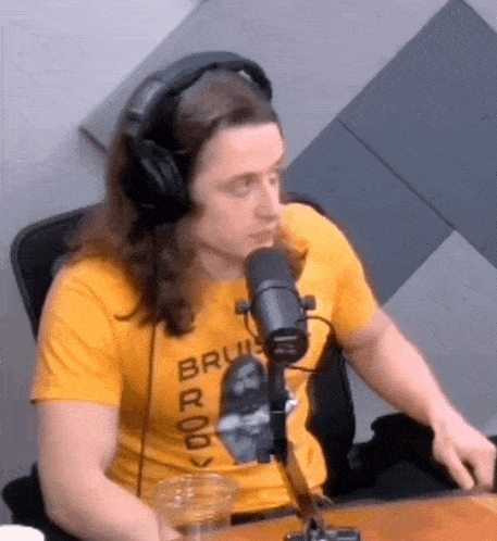 a man with long hair is wearing headphones and a yellow shirt while sitting in front of a microphone .