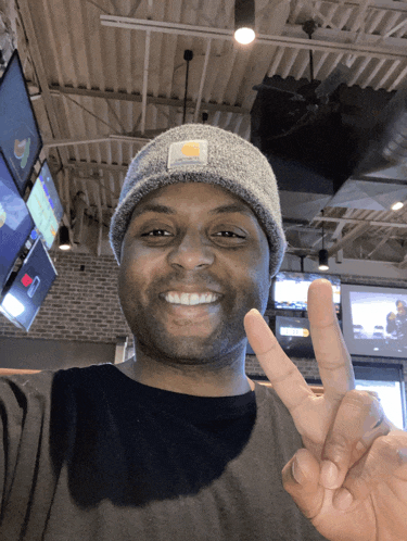 a man wearing a beanie and a black shirt giving the peace sign