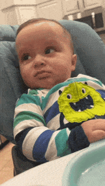 a baby sitting in a high chair wearing a striped shirt with a monster on it
