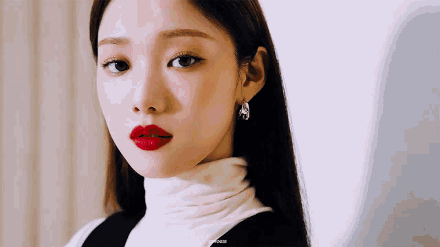 a woman wearing red lipstick and a white turtleneck looks at the camera