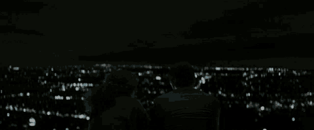 a man and a woman are looking at the city lights at night