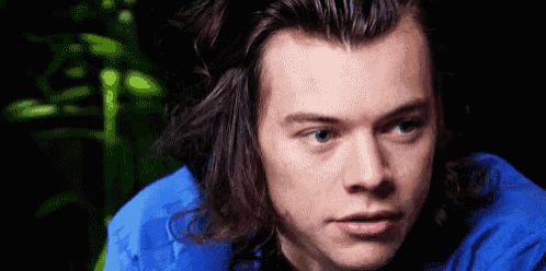 harry styles is wearing a blue shirt and has long hair .