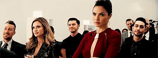 a group of people are sitting in a room with a woman in a red dress looking at the camera .