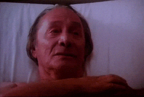 an elderly man is laying in a bed with his head on his arm