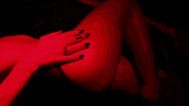 a woman in a black bra and black stockings is laying down in a dark room with a red light behind her .