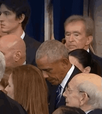 a man in a suit and tie is standing in a crowd of people and touching a woman 's face .
