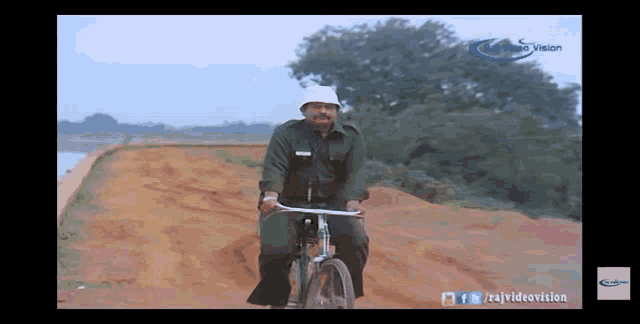 a man is riding a bike on a dirt road with the words raj video vision on the bottom left