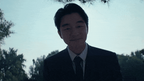 a man in a suit and tie stands in front of a tree