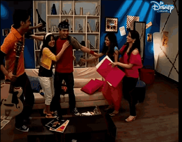 a group of people standing in a living room with a disney channel logo on the corner