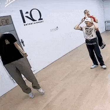 a man is carrying another man on his shoulders in a room with a ko entertainment logo on the wall