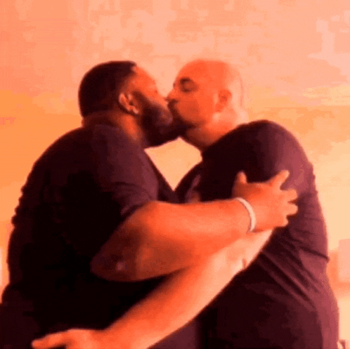 two men are hugging each other and kissing in front of a pink background .