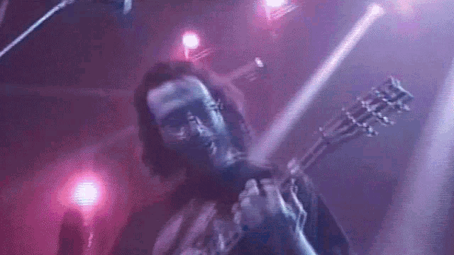 a man is playing a guitar in a dark room with purple lights