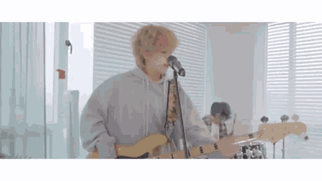 a young man is singing into a microphone while playing a guitar in a room .