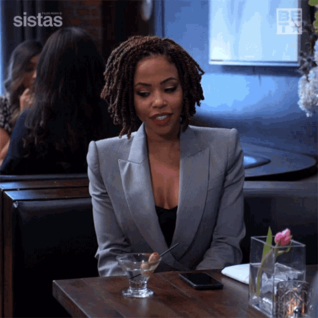 a woman is sitting at a table with a martini in front of her and the word sistas on the bottom